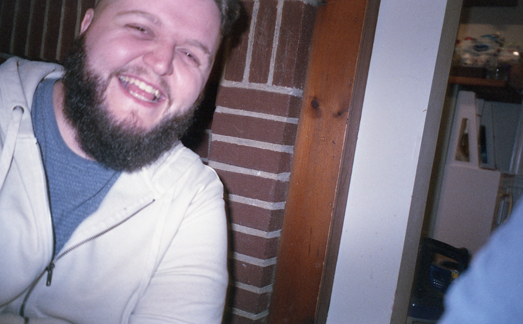 Polaroid of Ponders with camera around neck, leaning against a wall.