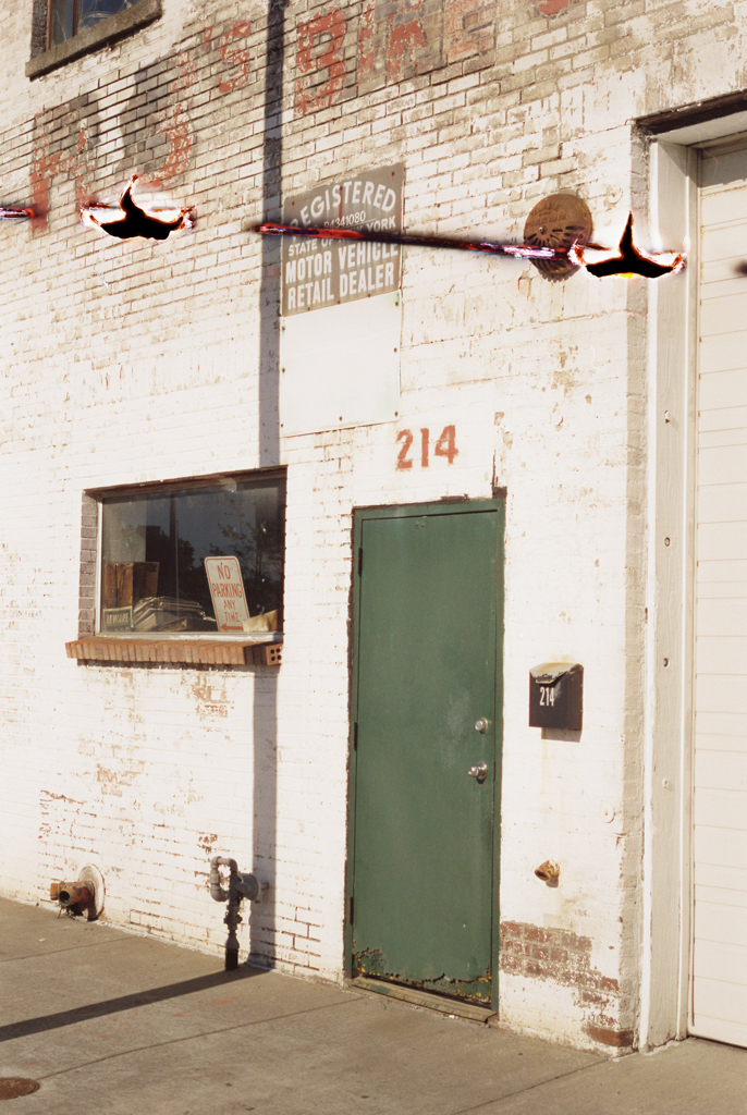 A green door in a white brick wall, with a small window next to it. It looks like an industrial workshop that's been closed. A tear from over-rolling the film left a scar along the upper third of the scan.