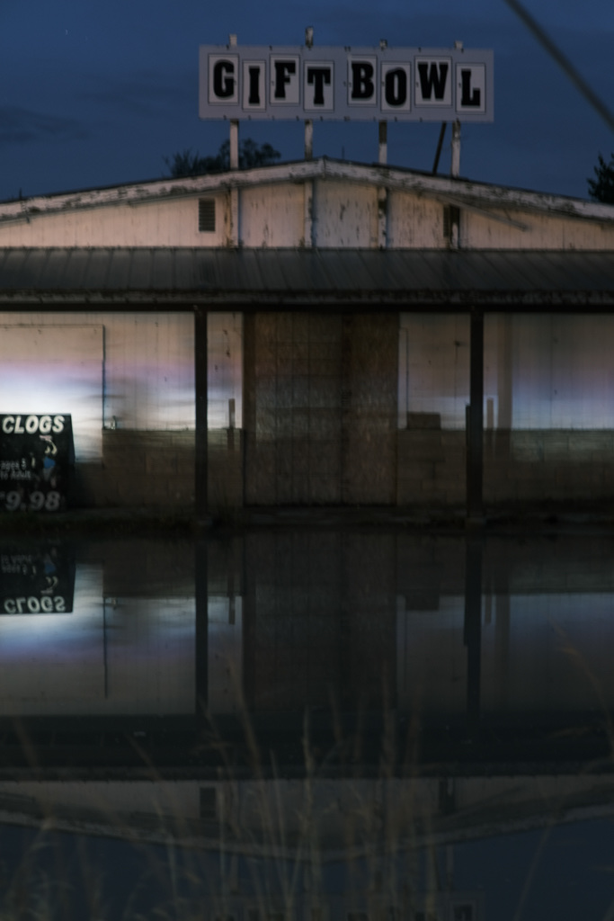 An abandoned bowling alley is perfectly reflected in the flooded parking lot.