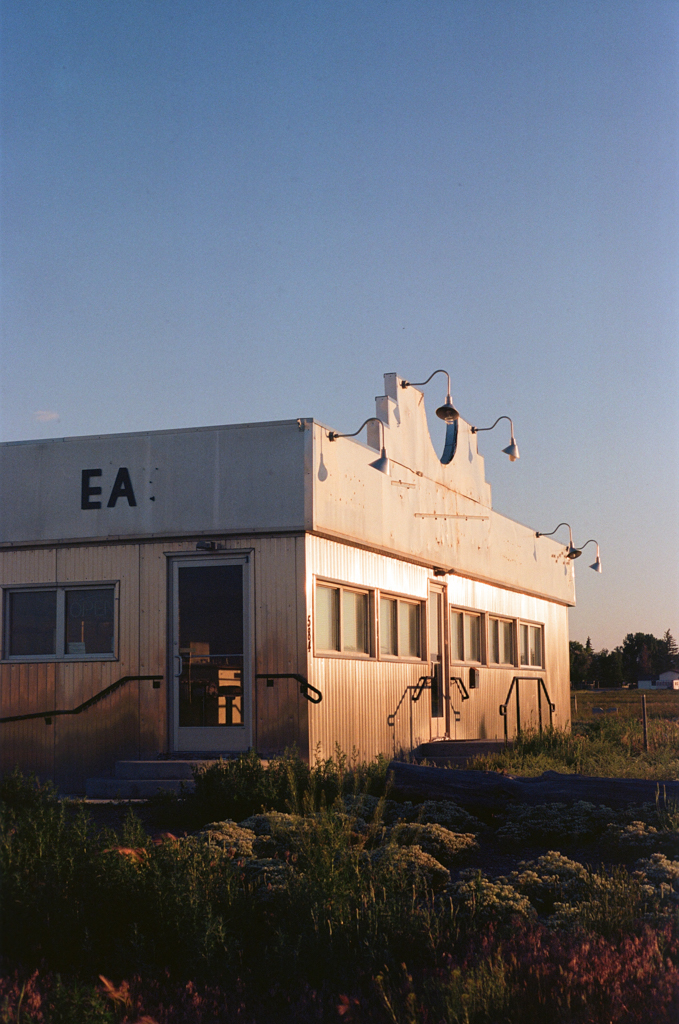 The sun rises over the abandoned Moondance Diner in La Barge, Wyoming. The letters 'E' and 'A' hang on the side of the building, and a faint outline reveals where the letter 'T' once was.